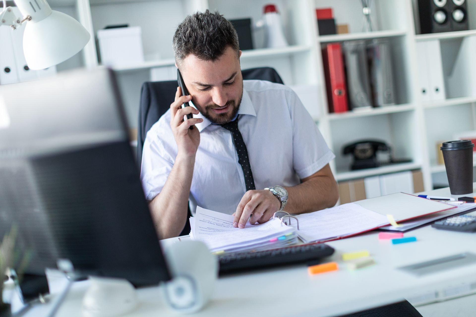 A man is sitting in the office, working with documents and talking on the phone. A man is sitting in the office, working with documents and talking on the phone.